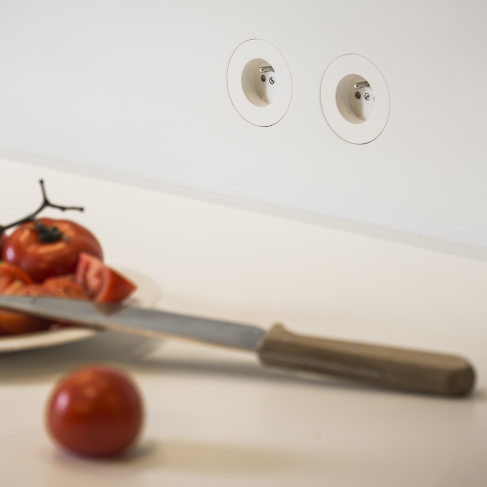 Prises de courant rondes, au niveau du plan de travail de la cuisine, s’intégrant parfaitement à la crédence en corian glacier white