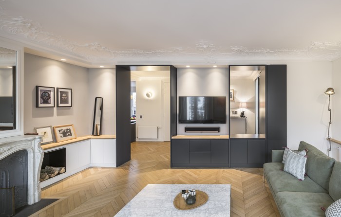 Le meuble sur mesure du salon intègre à la fois le champlat de l'ouverture nouvellement percée et un meuble tv. Ce travail d'ouverture laisse voir l'existence de plusieurs plans et arrières-plans dans l'appartement.