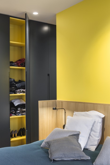 Tête de lit en chêne, adossée contre un mur jaune tournesol. Couleur qui se retrouve à l'intérieur des placard sur mesure, aux poignées en creux.
